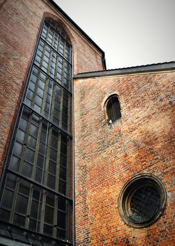 A tall leaded church window beside a round window in red brick.