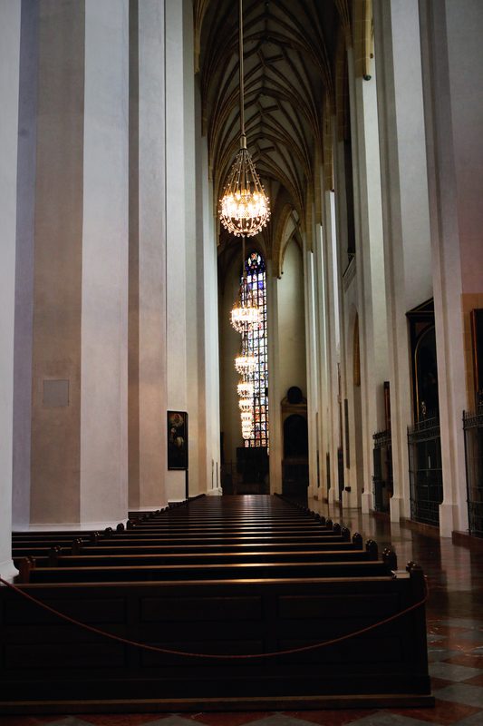 Tall white columns and a hanging chandelier down a church nave.