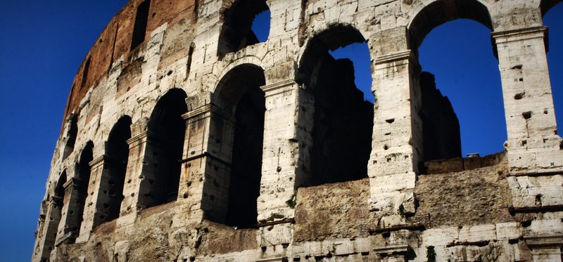 The Colosseum's upper arches with blue sky showing through.