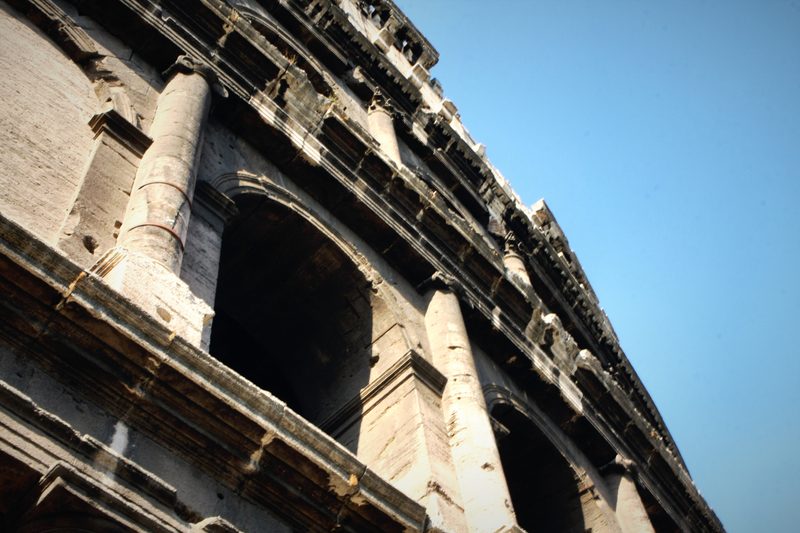 Colosseum arcades seen from below, climbing toward a blue sky.