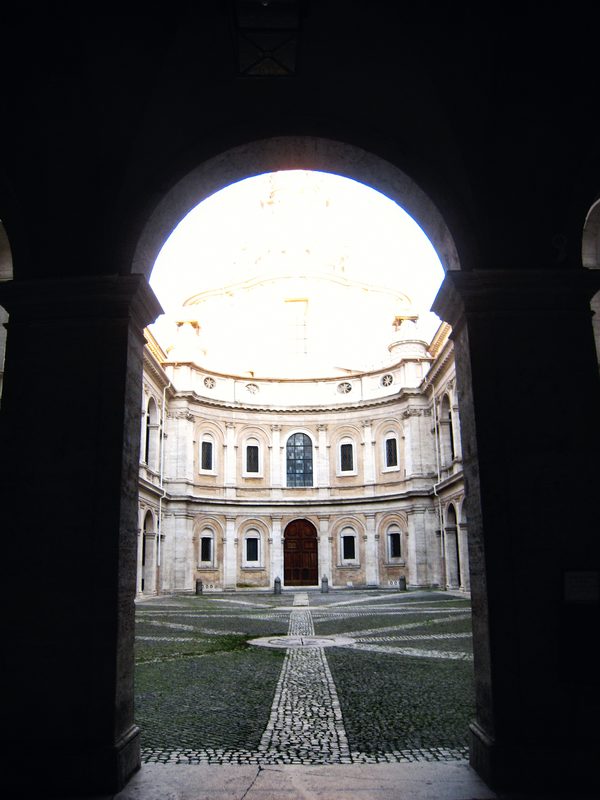 A dark archway framing a sunlit courtyard with an arcade beyond.