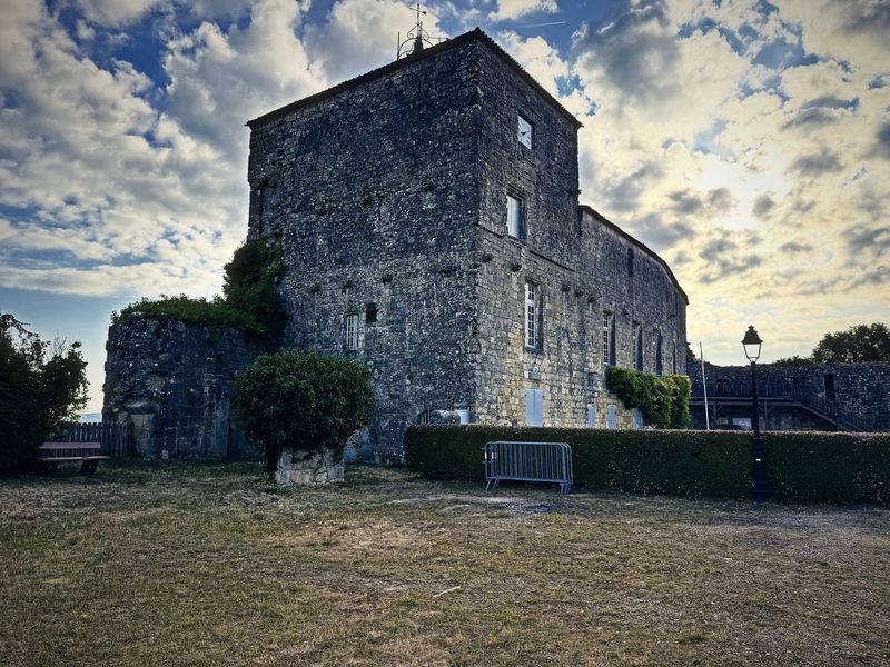 A square stone keep and its outbuildings under a dramatic sky of broken cloud.