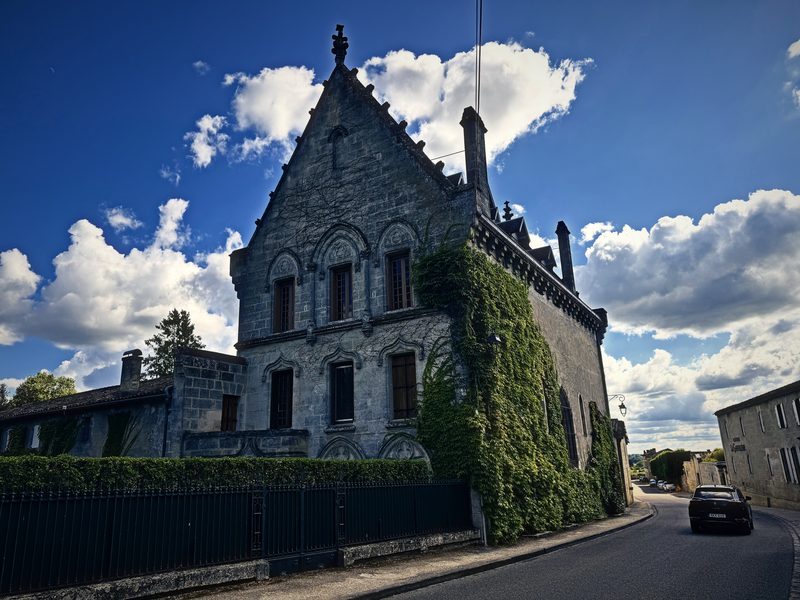 A steep-gabled Gothic house wrapped in ivy, set against blue sky and towering white clouds.