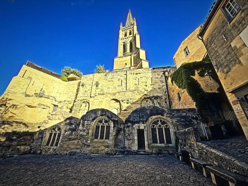 The rock-cut walls and arches of Saint-Émilion's Monolithic Church beneath its tall bell tower in morning sun.