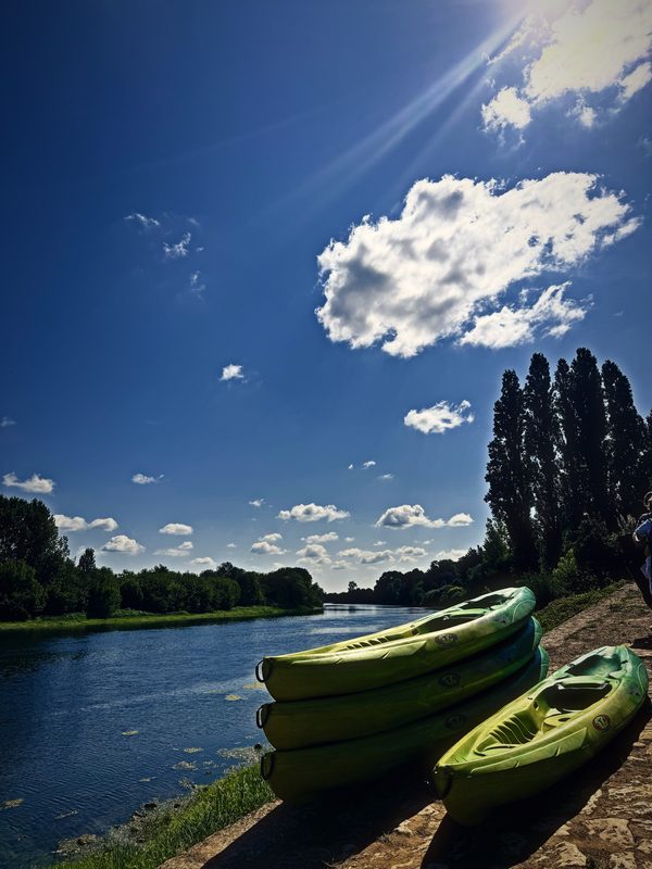 Green kayaks pulled up on the bank of the Dordogne beneath bright clouds and tall poplars.