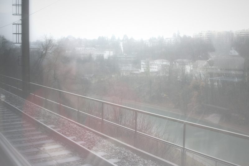 Misty view of a railing and a green hillside through a window.