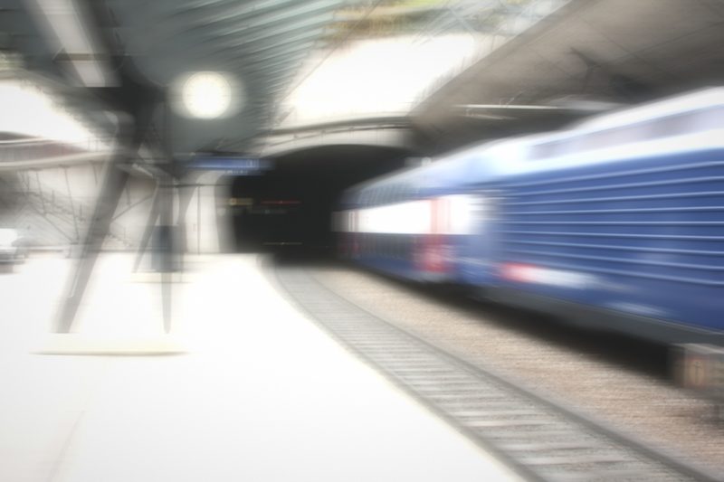 Hazy blue train entering a dark tunnel beside a bright platform.