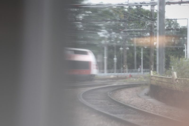 Dreamy view of a red train front rounding a curve, framed by a window edge.