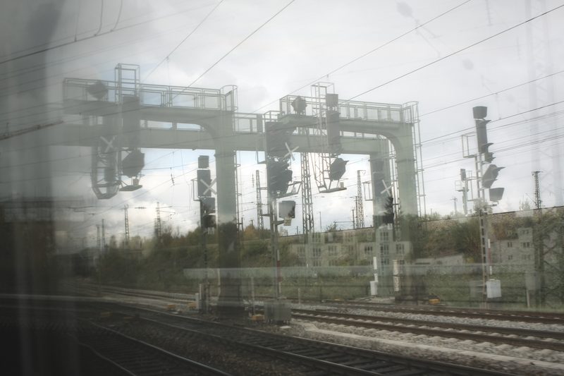 Double-exposed signal gantries and overhead wires over pale tracks.
