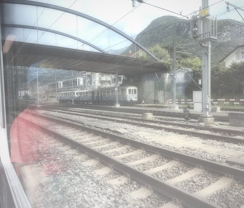 Soft reflection of a train in a glass shelter beside the tracks.