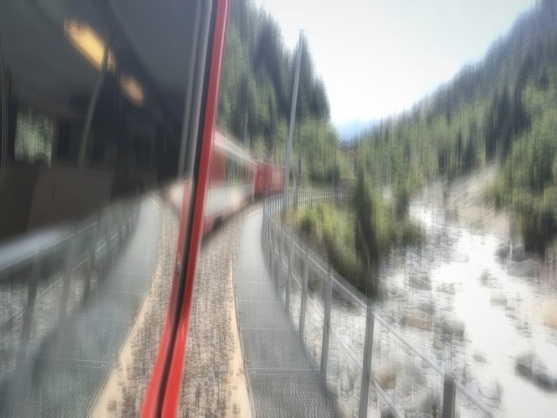 Hazy view of a mountain river and gorge from a train window with a red edge.
