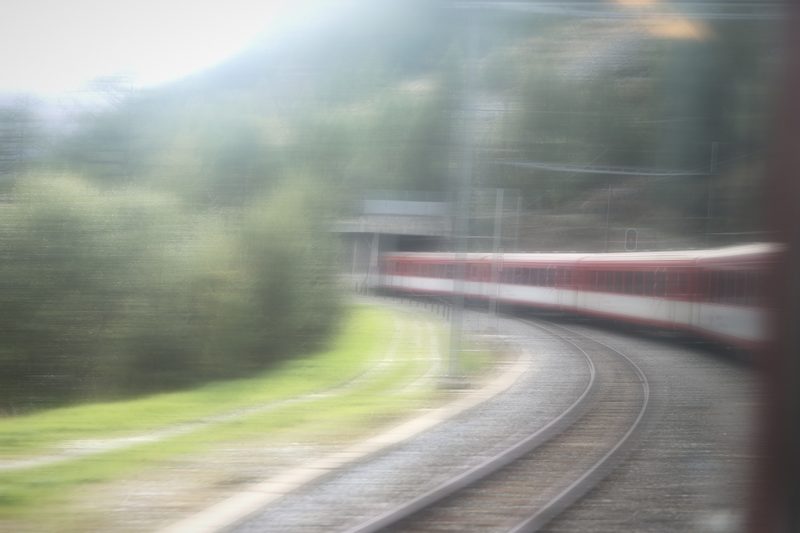 Dreamy blur of a red train curving through green trees.