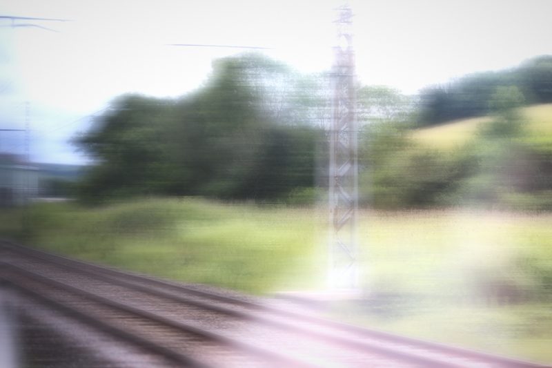 Pale motion blur of green fields and a pylon beside the tracks.