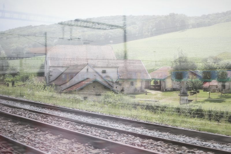 Double exposure of a farm village, fields and railway tracks in soft light.
