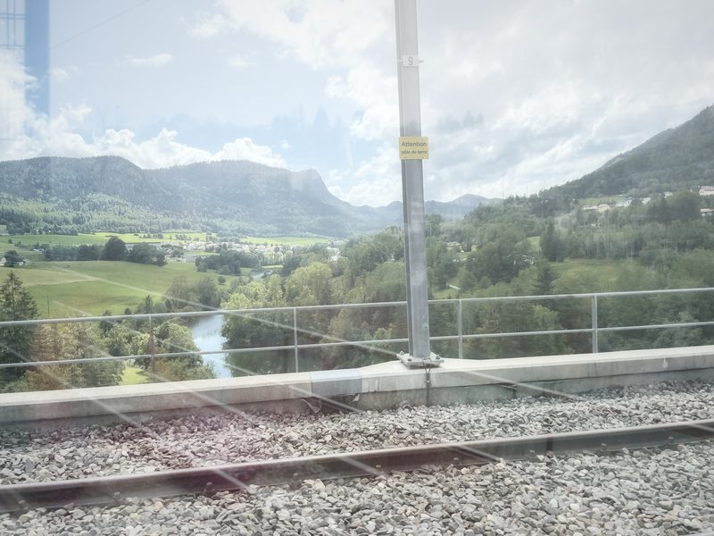 Double exposure of a green valley with a river, railing and tracks.