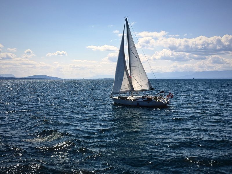 Sailboat heeling in the breeze on deep blue Lake Geneva under summer clouds.