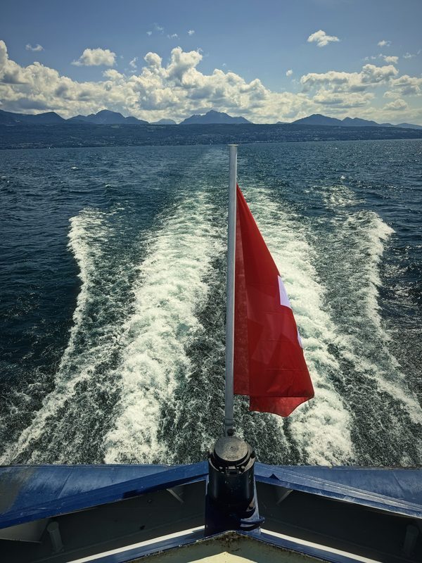 View from a boat's stern: a red flag over a wide white wake on Lake Geneva.