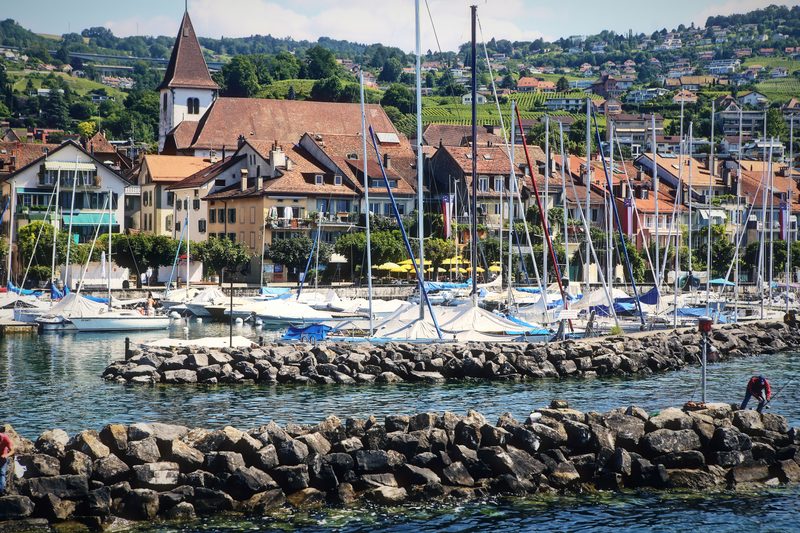Harbor full of sailboat masts below a church steeple and an old lakeside town.