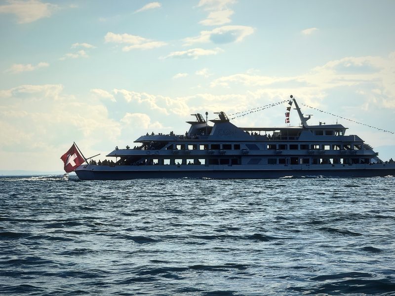 Sleek white lake cruiser with a Swiss flag sailing in early evening light.