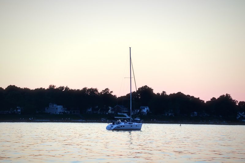 Lone sailboat silhouetted on calm water under a pink and lavender sky.