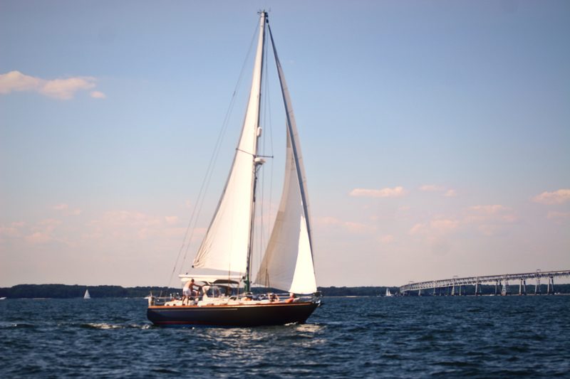 Sloop under full white sails on dark water in soft peach evening light.