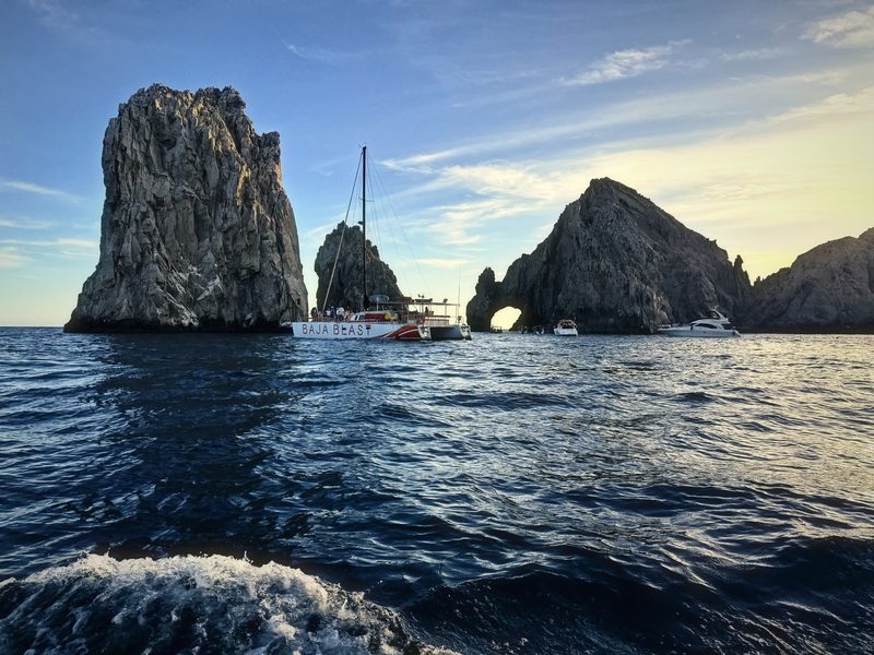 Granite sea stacks rising from the Pacific with a small sailboat among them.