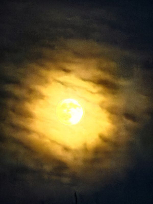 A full moon glowing gold through a ring of drifting cloud, the sky around it falling away to deep blue-black.