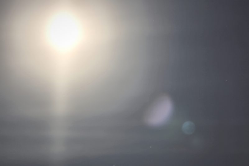 A blazing moon in a pale, misty sky above the sea, its light spilling down into soft haze.