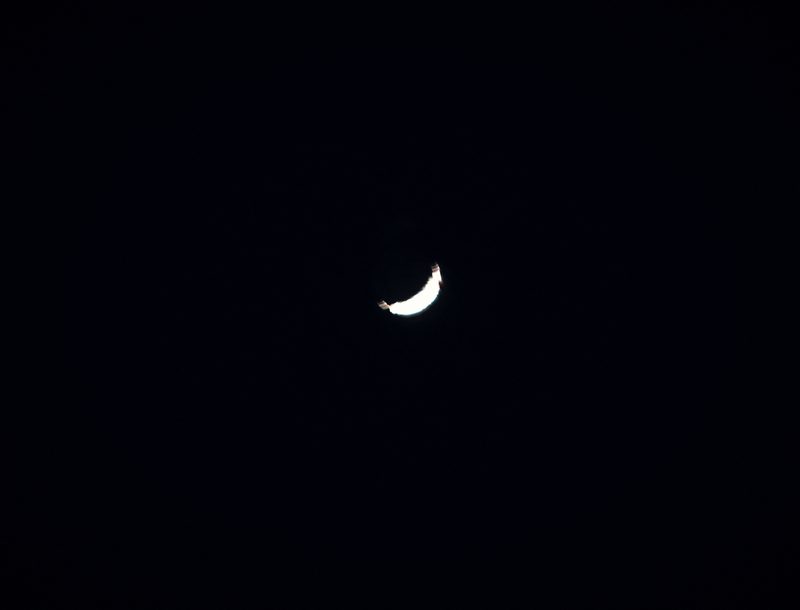 A delicate crescent moon, almost a hairline, alone in a black sky.