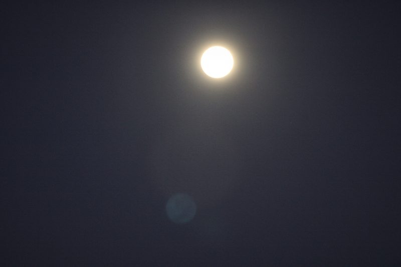 A bright full moon wrapped in a soft halo of light in a dark blue night sky.