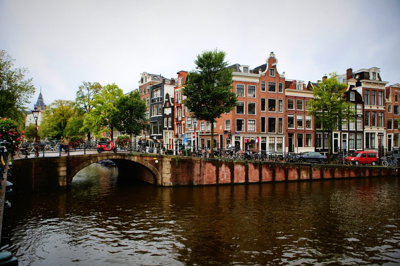A brick bridge with low arches spanning a canal in front of tall canal houses.
