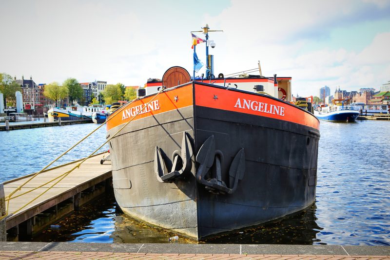 A black barge with an orange stripe moored on the waterfront.