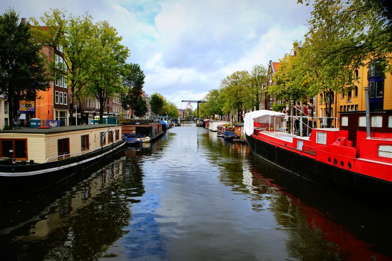 Houseboats moored along a tree-lined canal with a red boat on the right.
