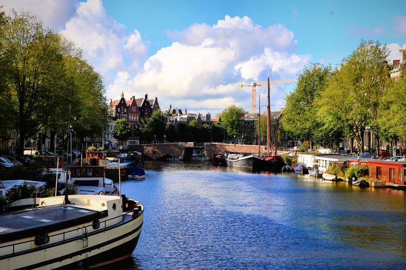 Wide water with houseboats and a lifting bridge under big clouds.