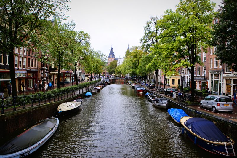 A long straight canal lined with trees and moored boats, a church tower at the far end.
