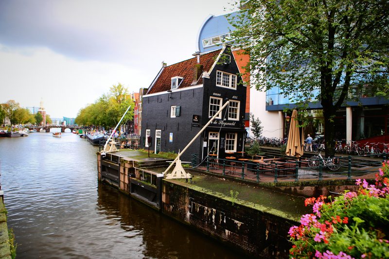 A dark wooden house by the water with pink flowers spilling over the quay.