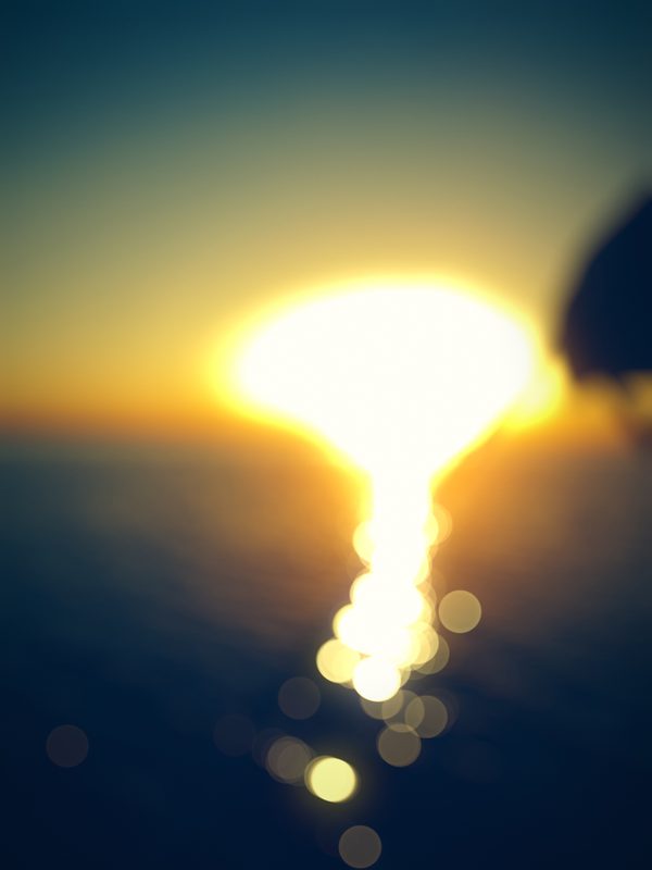 Setting sun and its reflection melting into gold bokeh over blue water.