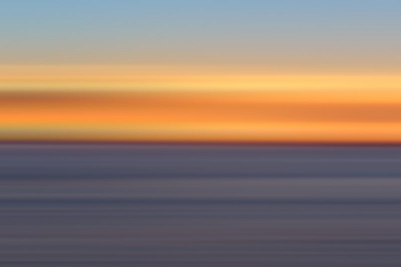 Horizontal color bands of tangerine, blue and slate from a sunset over the sea.