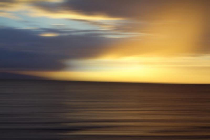 Long-exposure style abstract of golden sun rays breaking through dark clouds over the sea.