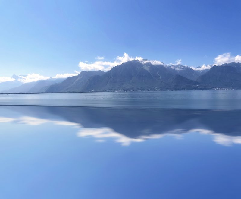 Mirrored lake and clouded mountain peaks in layers of blue.