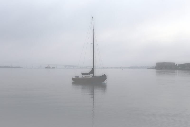 High-key misty image of a lone sailboat on pale water.