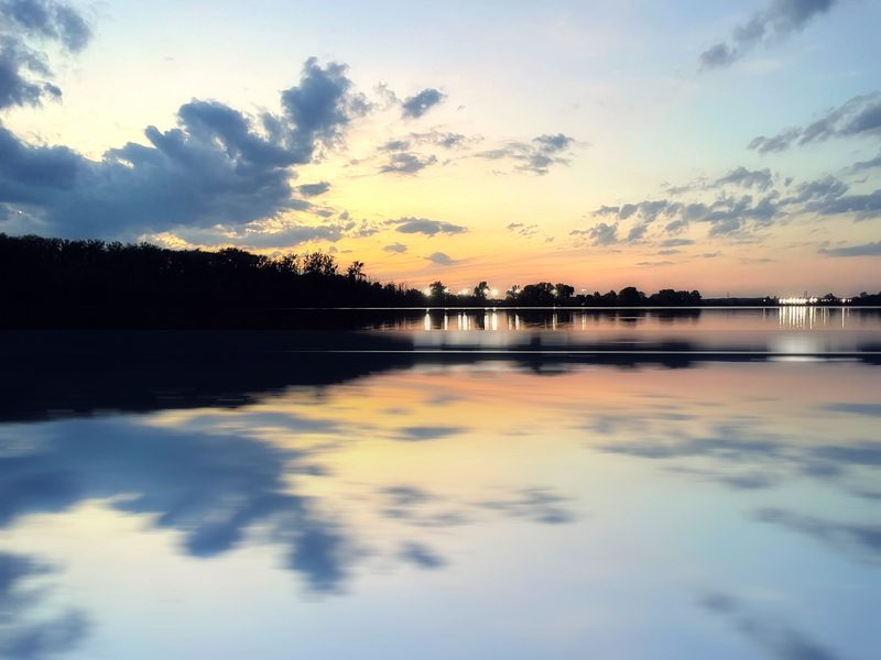 Symmetrical mirrored image of a glassy dusk lake, clouds and shoreline.