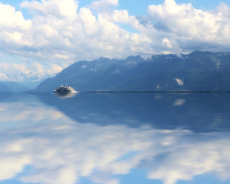 Mirrored image of the Alps and summer clouds reflected across Lake Geneva.