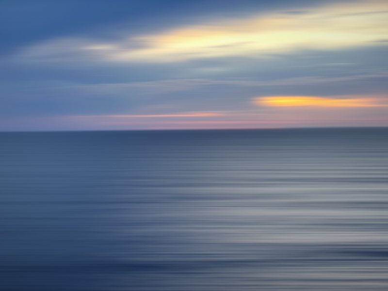 Smooth long-exposure style sea in deep blue with a thin warm band of light on the horizon.