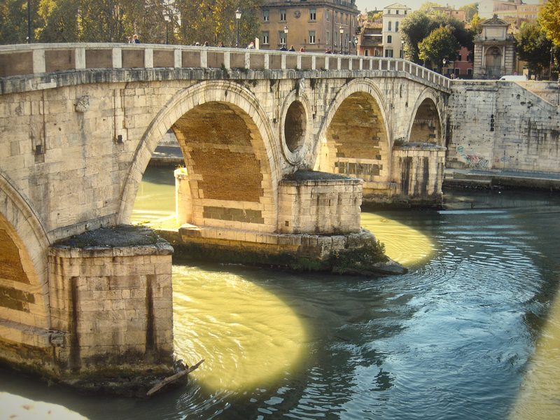The arches and round opening of Ponte Sisto reflected in the Tiber.
