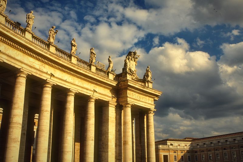 The columns and statues of St Peter's colonnade under dramatic clouds.