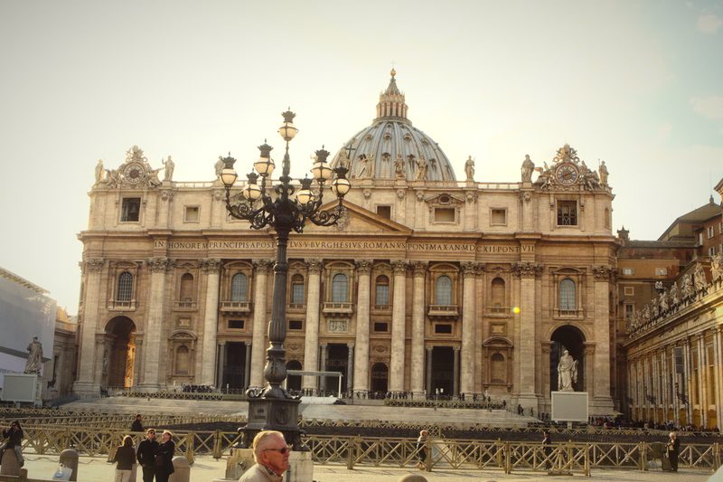The facade and dome of St Peter's Basilica with a lamp post in front.