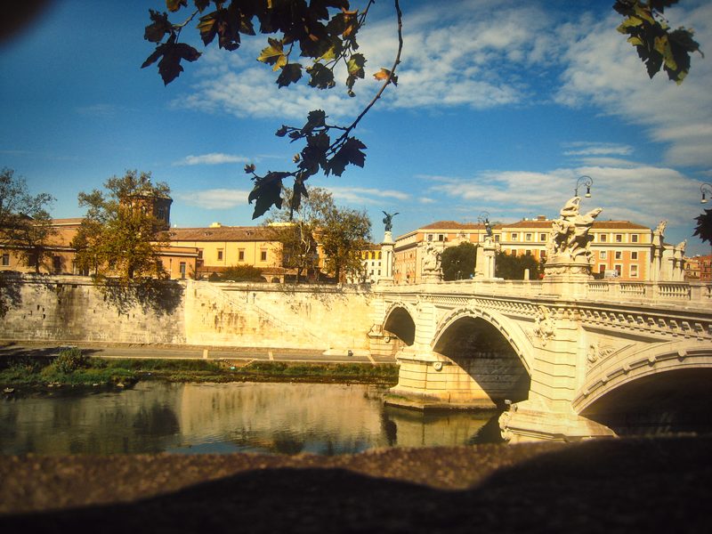 A stone bridge with statues over the Tiber, branches overhead.