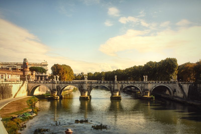 A long view down the Tiber to a many-arched bridge under a wide sky.