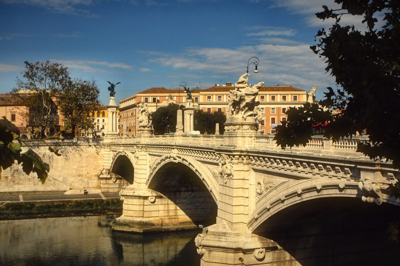 A bridge with statues and a domed building on the far side of the Tiber.